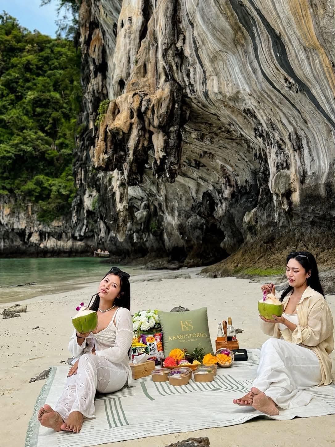 Guests with fresh coconuts on the sand below a limestone cliff